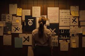 Le personnage de Lee est devant un mur d'indices contenent des lettres inventés.