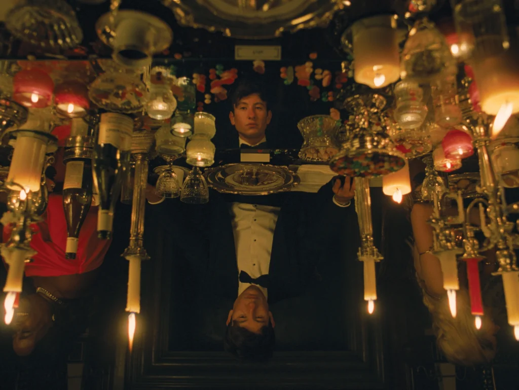 Le personnage d'Oliver est assis devant une table en miroir. Sur la table, il y a beaucoup de chandelles, de bouteilles et des bonbons.